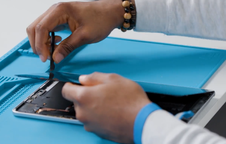Screenshot that shows a technician holding the display and inserting the Halberd Spudger knife edge into the bottom-right corner to cut through bottom-edge adhesive.