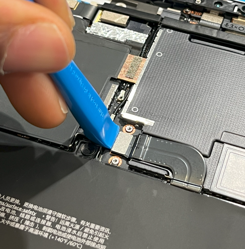 Screenshot that shows a hand using a tool to remove the battery connector bracket from the enclosure.