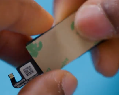 Photo that shows a person applying adhesive tape to the back of an NFC module using their fingertips.